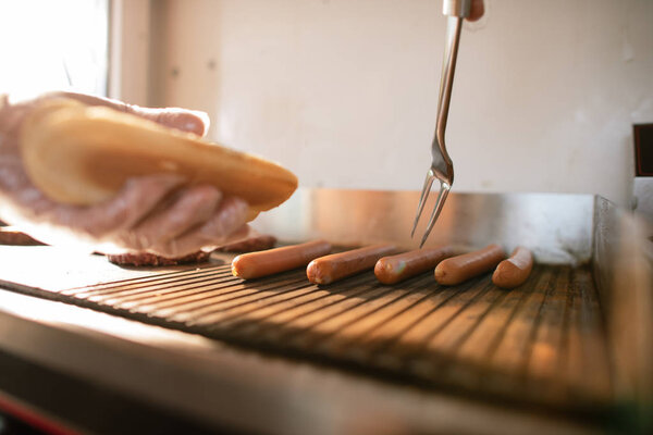 cropped image of chef preparing hod dog in food truck and taking sausage