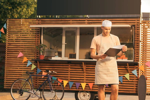 Knappe Chef Kok Schort Kijken Naar Klembord Buurt Van Voedsel — Stockfoto