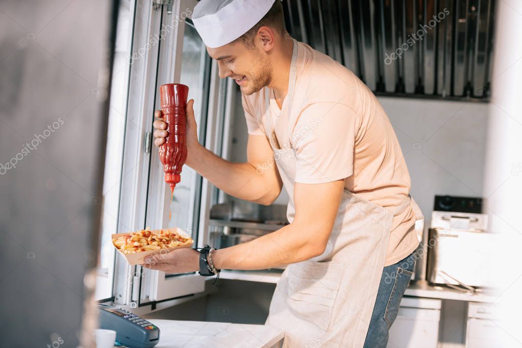 side view of chef adding ketchup to hot dog in food truck