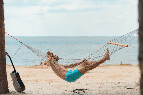 красивый бородатый мужчина лежит в гамаке на пляже рядом с морем
