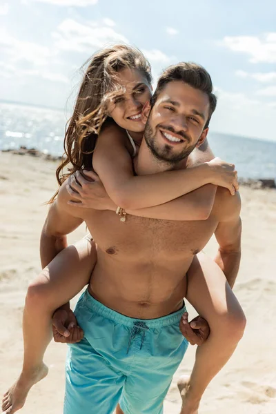 ビーチで彼のガール フレンドをピギーバック幸せな男 — ストック写真