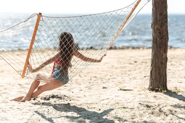 Vista Posteriore Della Ragazza Seduta Amaca Sulla Spiaggia Guardando Mare — Foto stock gratuita