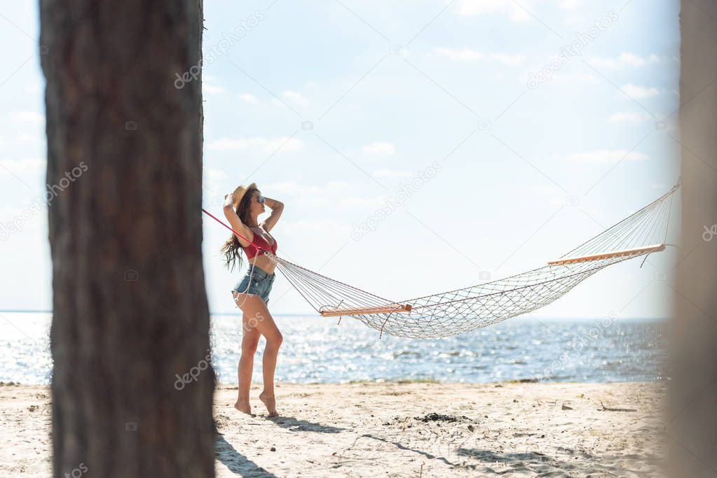 girl in straw hat posing on sea beach with hammock and blue sky