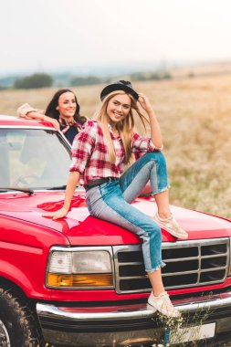 attractive young girlfriends having car trip and relaxing in flower field clipart