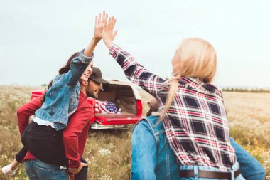 rear view of young women piggybacking on boyfriends and giving high five in flower field clipart