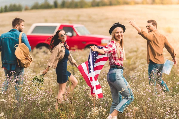 一群快乐的年轻的美国汽车旅行者与旗帜走在花卉领域 — 图库照片