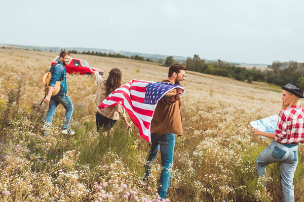 group of happy young american travellers with flag walking by flower field