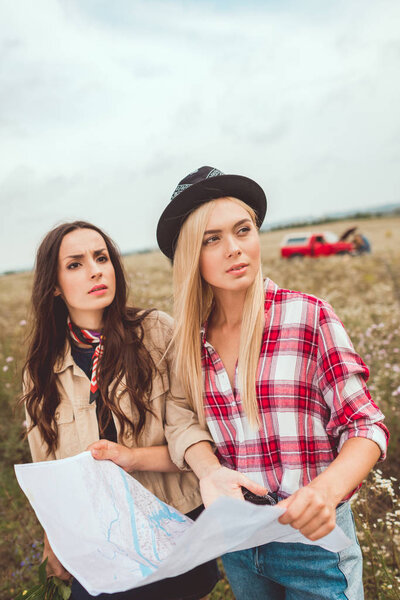 young girlfriends with map standing in field and trying to navigate