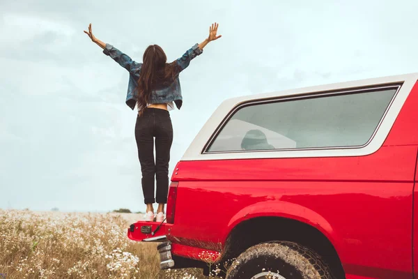 花畑で車のトランクに立っている若い女性の背面図 — ストック写真