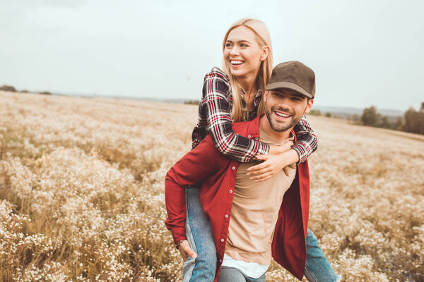 happy young woman piggybacking on boyfriend in flower field