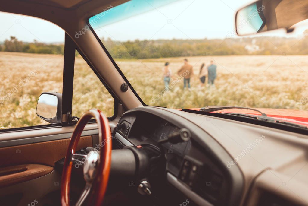 vintage car interior with people walking by flower field during car trip blurred on background