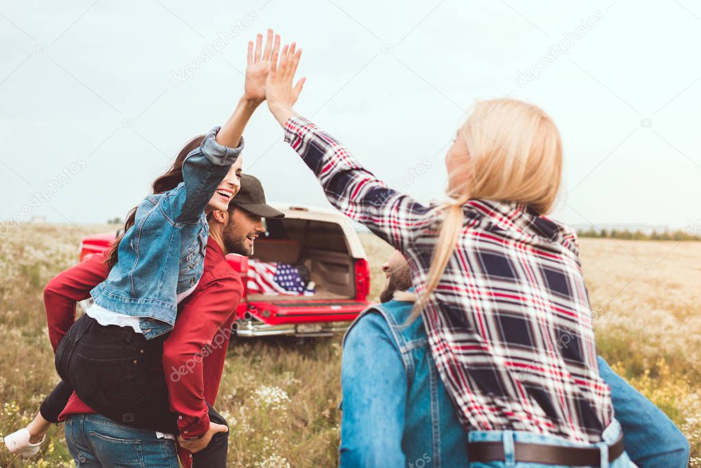 rear view of young women piggybacking on boyfriends and giving high five in flower field