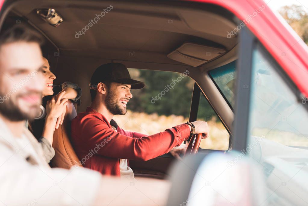 happy young friends travelling by car and riding by flower field