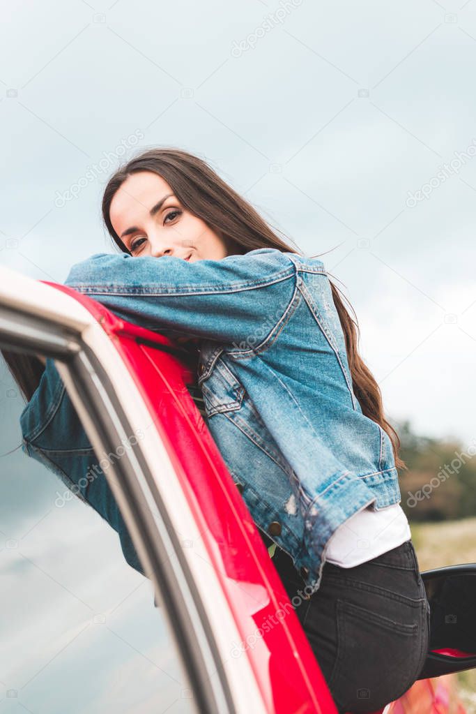 beautiful young woman leaning on red vehicle outdoors and looking at camera