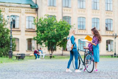 students with bicycle and notebooks standing on street near university clipart