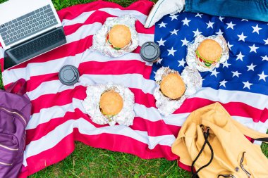 yeşil çimenlerin üzerinde gitmek Amerikan bayrağı laptop, hamburger ve kahve ile yatan adam kısmi görünümünü