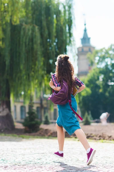 バックパックとノートブックの通りに実行している若い学生の背面図 — ストック写真