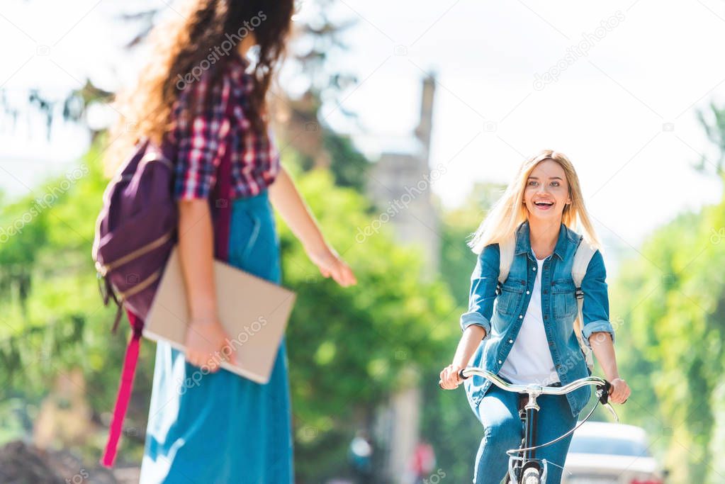 happy student looking at classmate while riding bicycle on street