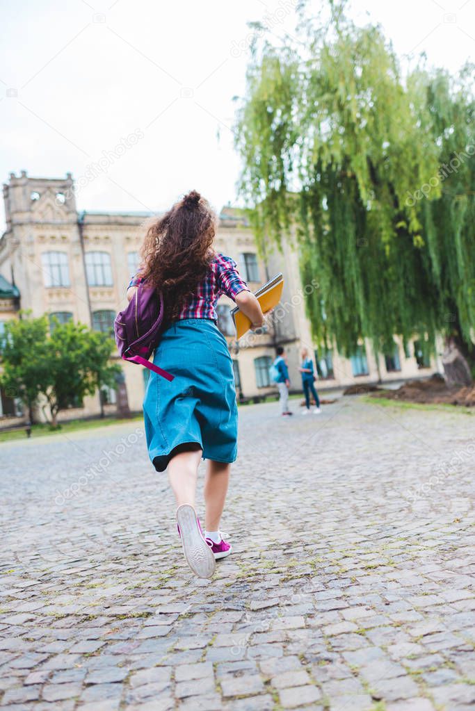 back view of young student with backpack and notebooks running on street