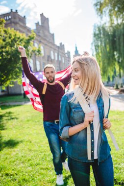 selective focus of smiling woman and boyfriend with american flag in hands in park clipart