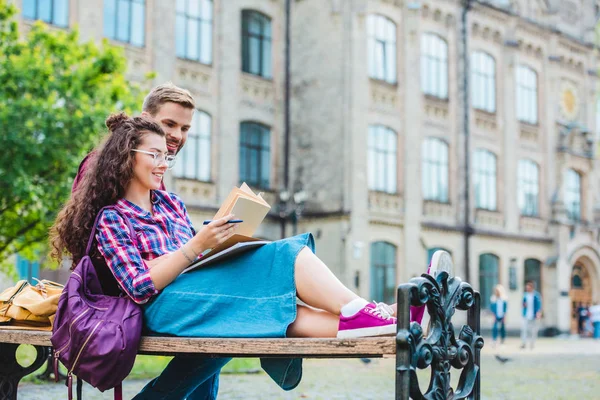 Усміхнена Молода Жінка Книгою Блокнотом Спирається Хлопця Дерев Яній Лавці — стокове фото