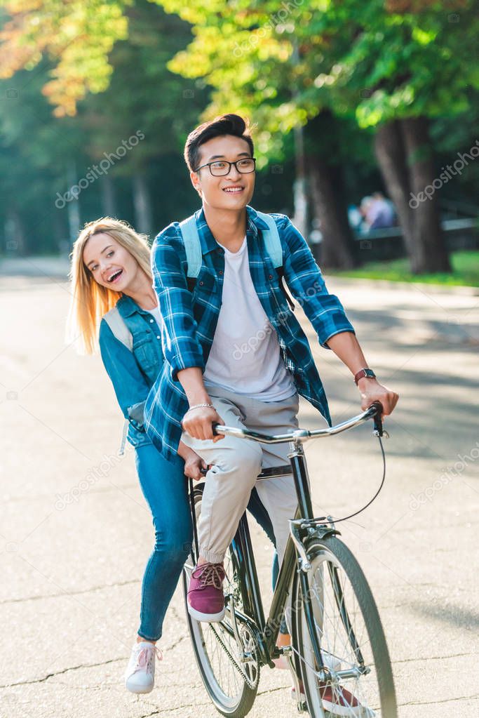 happy multiethnic students riding bicycle together on street