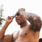 Vista de ángulo bajo de hombre tatuado muscular quitándose las gafas de sol