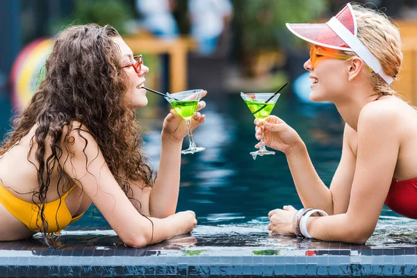 Vista Lateral Dos Atractivas Amigas Sonrientes Bebiendo Cócteles Piscina — Foto de Stock