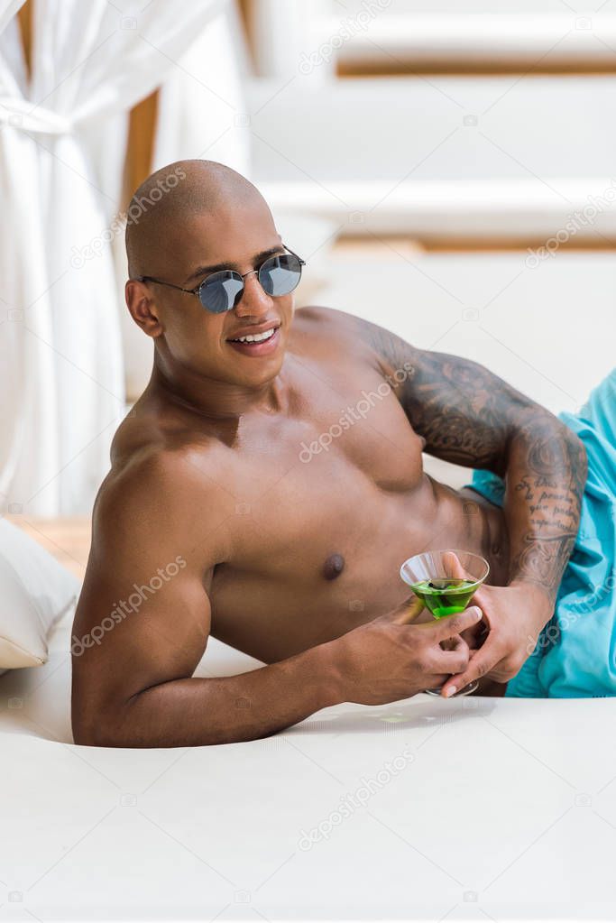 shirtless tattooed muscular man lying on sun lounger with cocktail