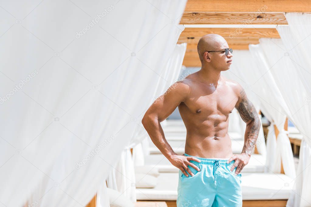 tattooed sportive man standing near sun loungers and looking away
