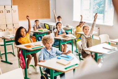 group of pupils raising hands to answer question during lesson at classroom clipart