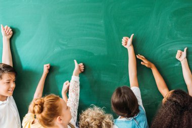 cropped shot of schoolchildren showing thumbs up in front of blank chalkboard clipart