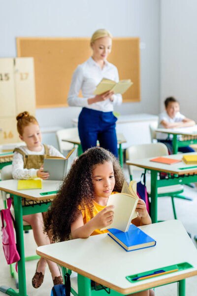 teacher reading book with children during lesson