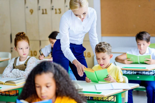 Hermosa Maestra Chequeando Cómo Los Niños Leen Libros Durante Lección — Foto de Stock