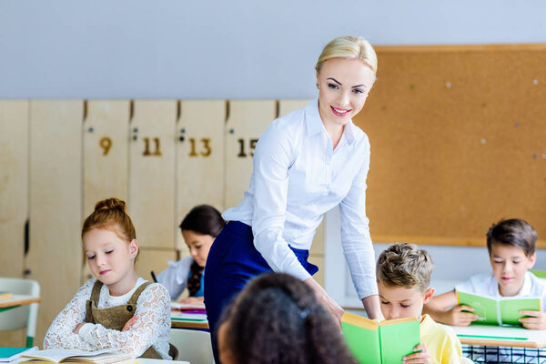 happy teacher checking how kids reading books during lesson