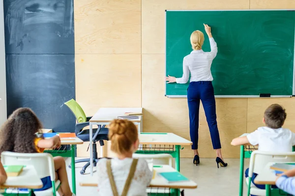 Rückansicht Von Schülern Die Lehrerin Beim Schreiben Auf Kreidetafel Anschauen — Stockfoto