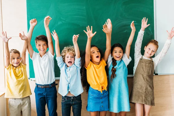 Adorable Happy Schoolchildren Raised Hands Standing Front Blank Chalkboard — Stock Photo, Image