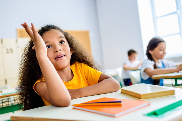 Африканская американская школьница поднимает руку, чтобы ответить на вопрос учителей во время урока
