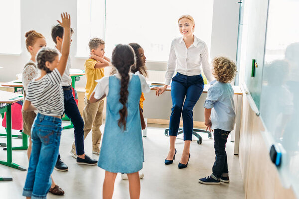 group of classmates standing around teacher at classroom and having fun