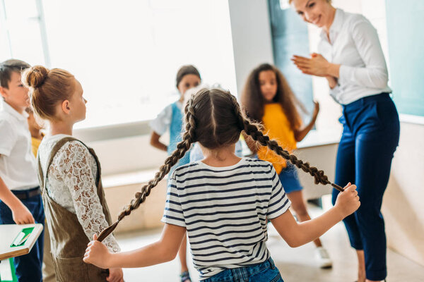 group of multiethnic classmates standing around teacher at classroom