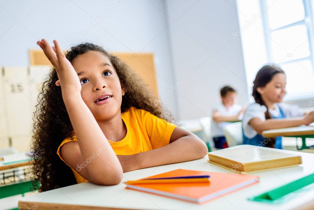 african american schoolgirl raising hand to answer teachers question during lesson