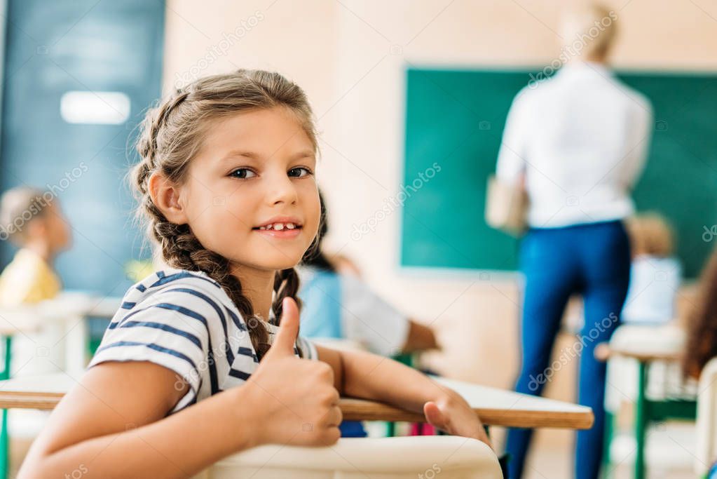 adorable little schoolgirl showing thumb up at camera during lesson