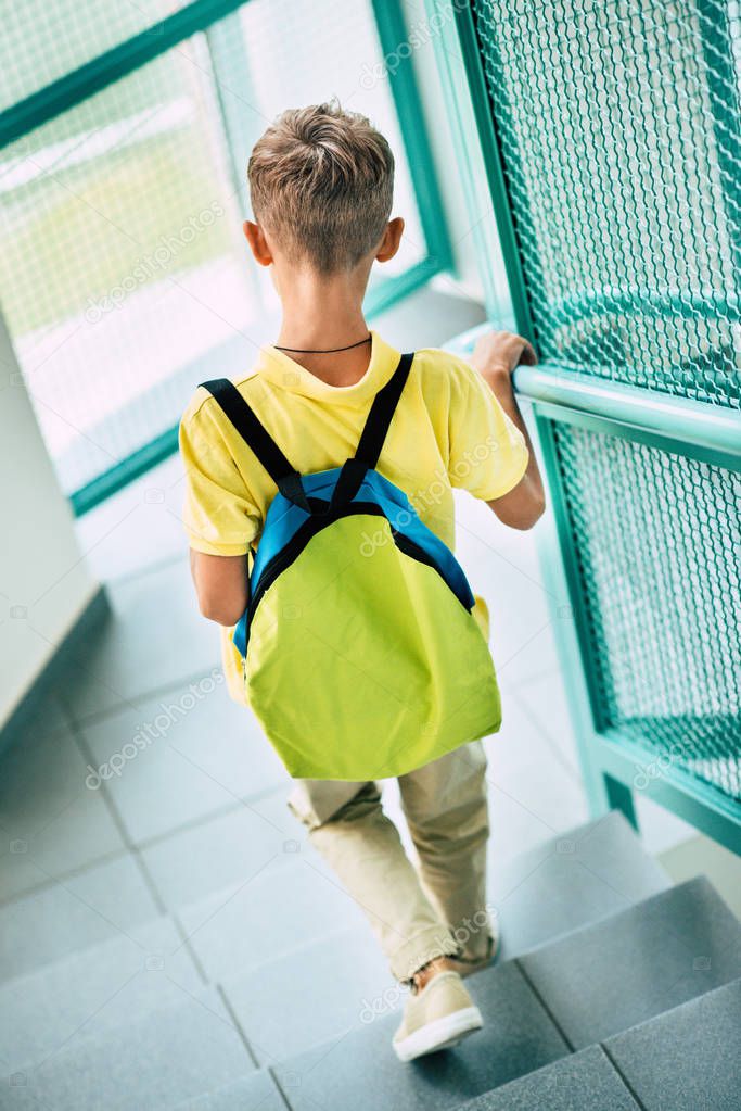 rear view of schoolboy with backpack going downstairs at school corridor