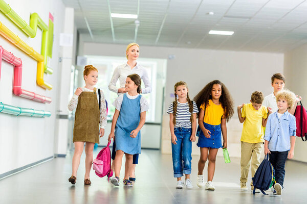 group of happy multiethnic classmates walking by school corridor