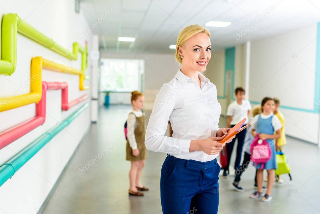 beautiful smiling teacher standing at school corridor with children on background