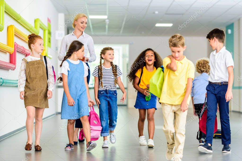 group of happy classmates walking by school corridor