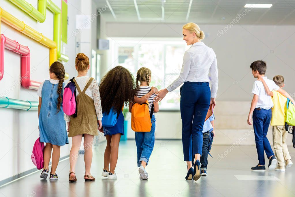 rear view of group of schoolchildren and teacher walking by school corridor