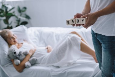 Bebek hamile eşi evde koltukta istirahat ederken yazı ile ahşap bloklar tutan adamın kırpılmış atış