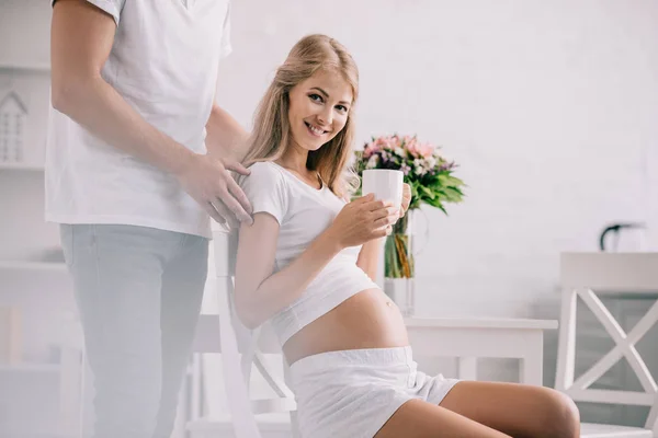 Částečný Pohled Usmívající Těhotná Žena Šálek Čaje Židli Manželem Poblíž — Stock fotografie