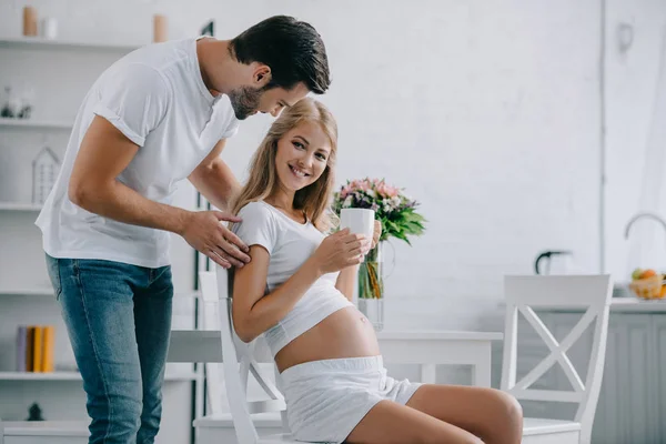 Usmívající Těhotná Žena Šálek Čaje Židli Manželem Poblíž Tím Doma — Stock fotografie